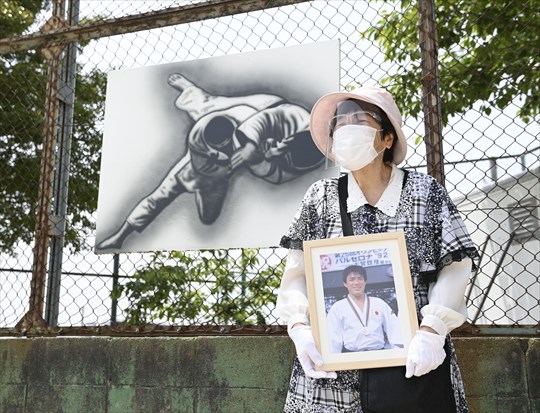 佐賀県みやき町の聖火リレー会場で、古賀稔彦さんの写真を抱き開始を待つ母愛子さん=10日午前