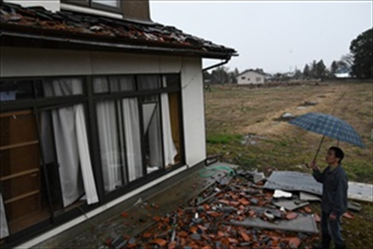 瓦が落ち、ガラス窓が割れたままの自宅を見つめ、被害拡大を心配する望月さん=18日、桑折町