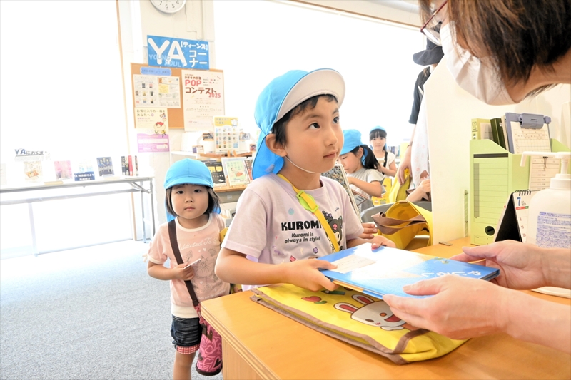 図書館のカウンターで気に入った本を借りる園児