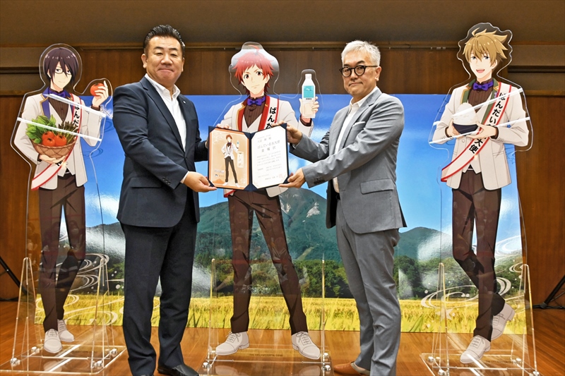 「ばんだい名水大使」に就いた3人のパネルの前で、浜取締役に委嘱状を手渡す佐藤町長(左)