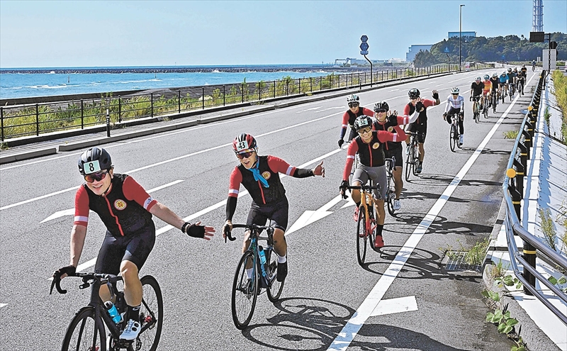 県道広野小高線(浜街道)を疾走するふくしま復興ライド120の参加者。右後方は東京電力福島第2原発=6日午前8時30分ごろ、富岡町