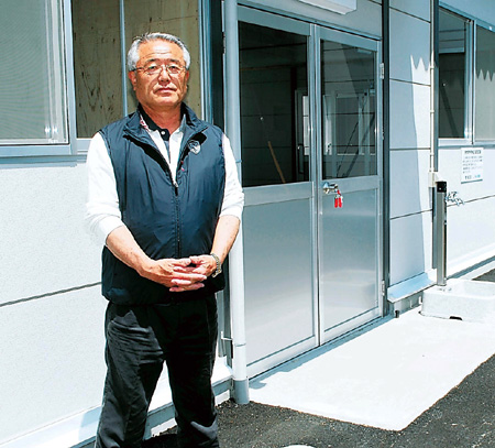 プレハブの仮設店舗前に立つ山田さん