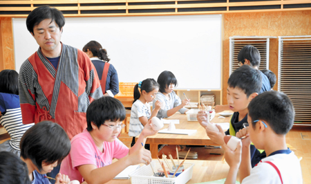 「風と土の芸術祭」に向け、児童に作品作りを指導する西田さん（左）