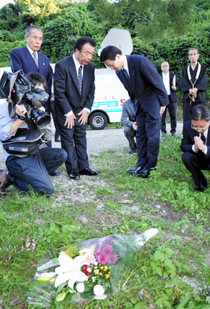 はま子さんが焼身自殺した現場に花を手向け、幹夫さん（中央左）に頭を下げる近藤室長（同右）。手前右は島田副室長