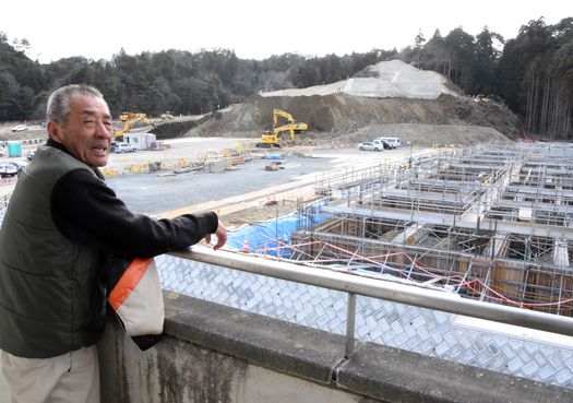 建設が進む豊間中を前に古里復興への思いを語る鈴木さん